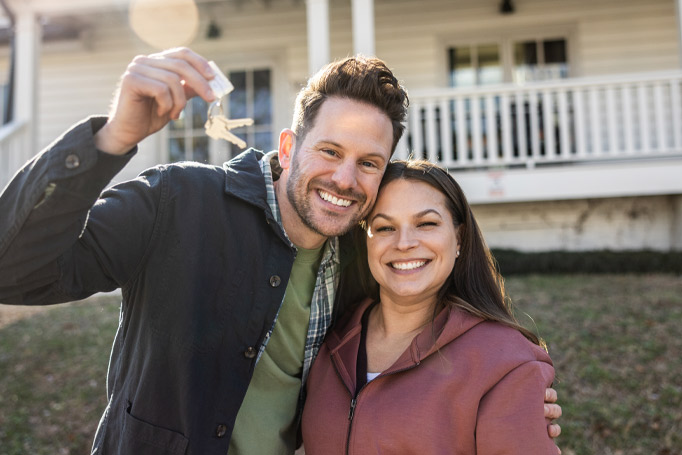 A couple standing outside their house with the man holding up the house keys
