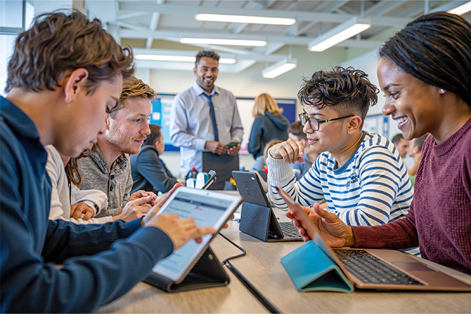 Group of students sitting together working on their laptops while teacher is watching