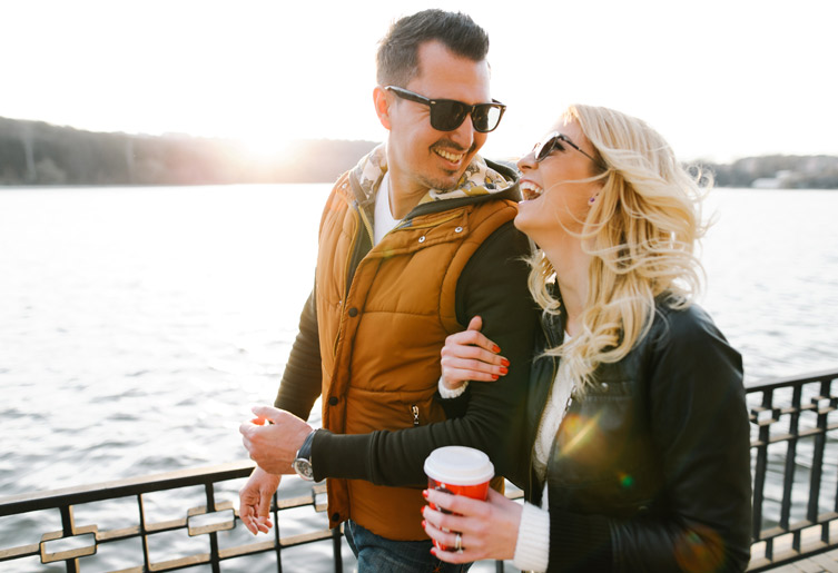 Couple standing together near a lake with woman holding a cup of coffee