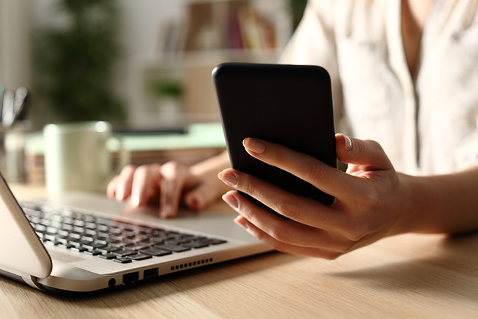 Woman holding her phone and using laptop with other hand to check bills