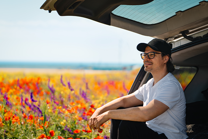 man sitting in car in field of flowers